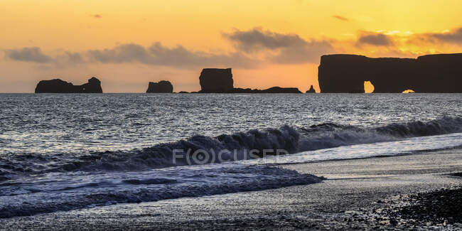 Рейхаара, базальтовые скальные образования у побережья и пляж с черным песком на закате; Мирдалшреппур, Южный регион, Исландия — стоковое фото