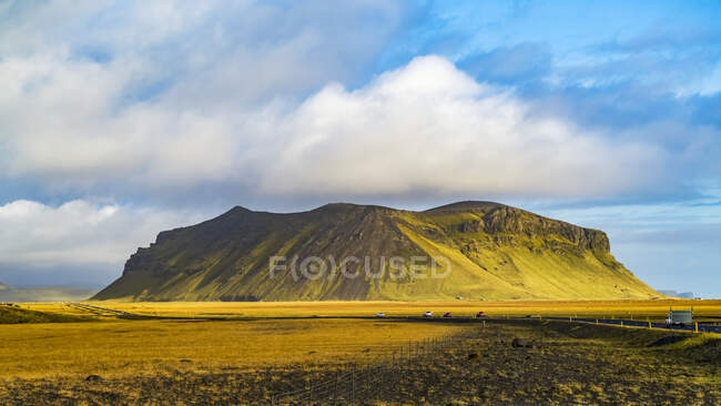Жорстка огорожа, вкрита зеленою тундрою, і дорога, що пролягає через безкраї краєвиди; Ісландія — стокове фото