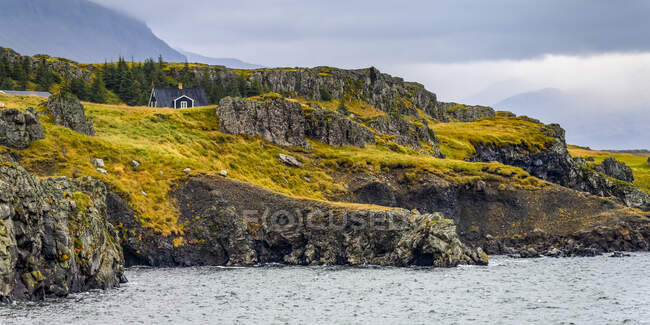 Ein Haus versteckt vor der zerklüfteten Küste am Fjord Berufjorour in Ostisland; Djupivogur, Östliche Region, Island — Stockfoto