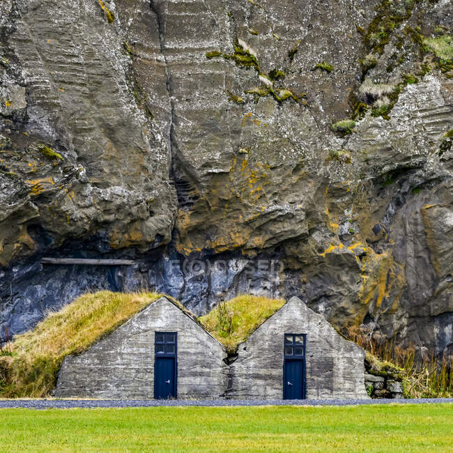 Two indentical houses with blue doors and grass roofs built into the rock of a mountainside; Rangarping eystra, Southern Region, Iceland — Stock Photo