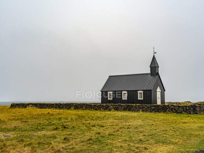 Edificio de la iglesia con campanario y cruz en una zona remota con muro de piedra y hierba; Snaefellsbaer, Región occidental, Islandia - foto de stock