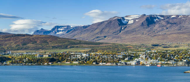 Town in Iceland with bright blue water and mountains having traces of snow on the peaks; Iceland — Stock Photo