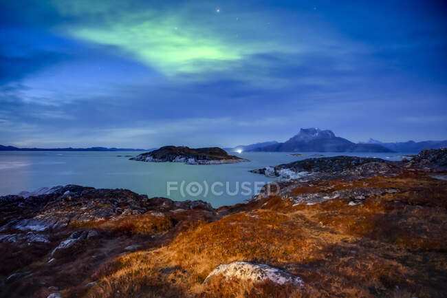 Die Nacht bricht über die zerklüftete Küste Grönlands herein, mit einem grünen Leuchten am Himmel, das sich im ruhigen Wasser darunter widerspiegelt; Nuuk, Sermersooq, Grönland — Stockfoto