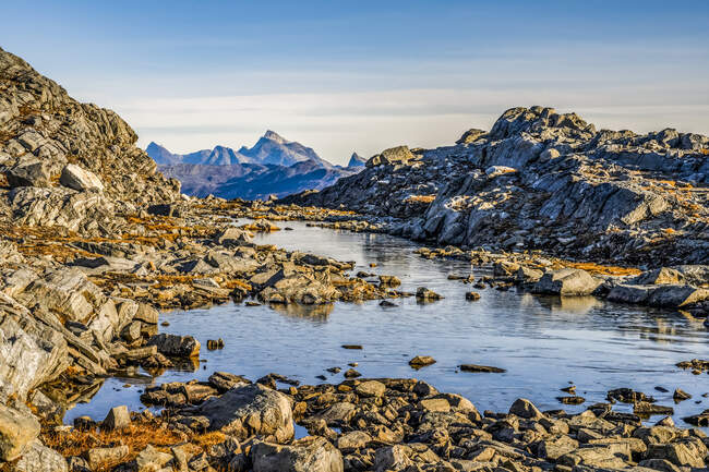 Скелястий пейзаж з водою і суворими гірськими вершинами на відстані; Сермерсук, Гренландія. — стокове фото