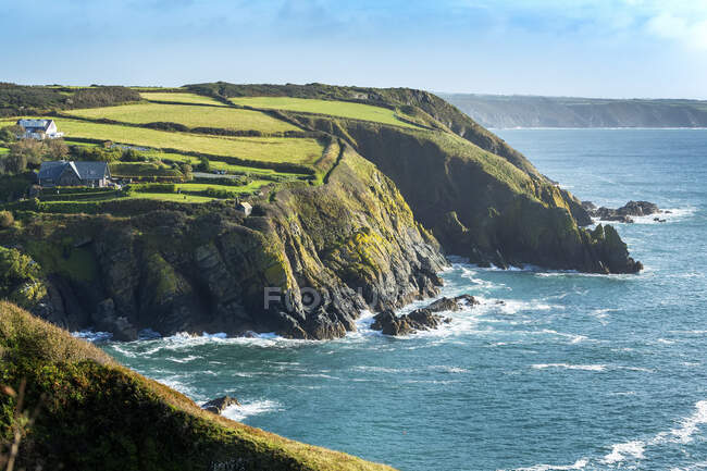 Rocky cliff shoreline with patchwork green fields and blue sky; Cornwall County, England — Stock Photo