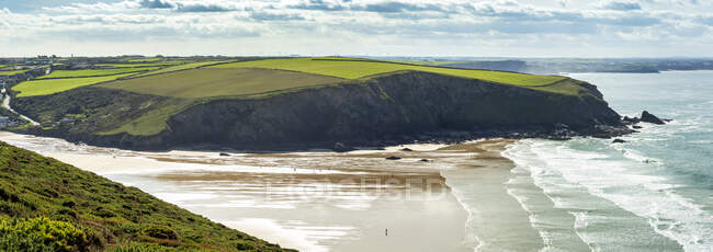 Péninsule côtière rocheuse avec un patchwork de champs verts, de plages et de vagues en dessous, ciel bleu et nuages ; comté de Cornwall, Angleterre — Photo de stock
