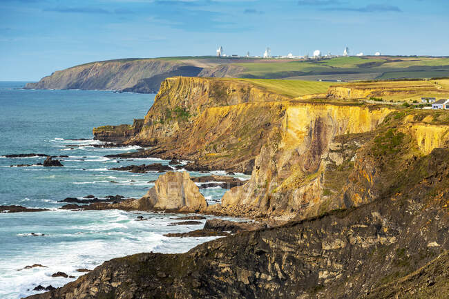 Dramatique rivage rocheux falaise avec la lueur du coucher de soleil avec de grandes antennes paraboliques blanches en arrière-plan ; Comté de Cornwall, Angleterre — Photo de stock