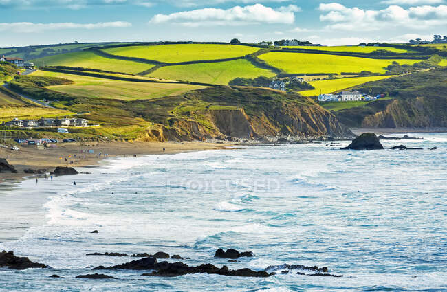 A patchwork of hilly fields bordered by trees and shrubs along the cliffs with blue sky and clouds; Cornwall County, England — Stock Photo