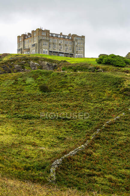 Un château de pierre au sommet d'une colline couverte d'arbustes et d'un mur de pierre ; comté de Cornwall, Angleterre — Photo de stock