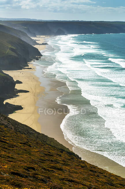 Playas de arena con olas a lo largo de una costa cubierta de hierba con cielo azul y nubes; Condado de Cornwall, Inglaterra - foto de stock