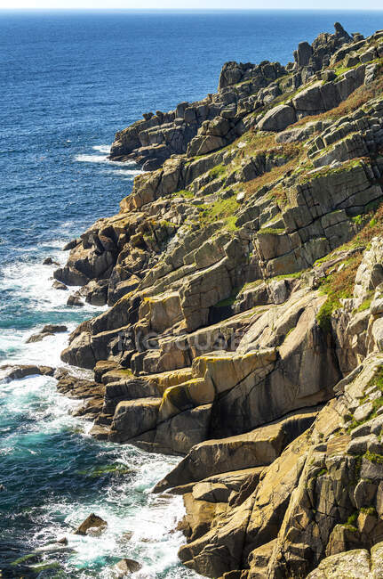 Rocky cliffs along the shoreline with surf and blue sky; Cornwall County, England — Stock Photo