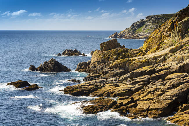 Formaciones de acantilados rocosos a lo largo de la costa con cielo azul y nubes; Condado de Cornwall, Inglaterra - foto de stock