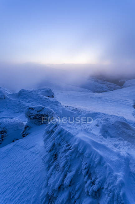Rocas cubiertas de nieve en las montañas Galty en invierno al amanecer con nubes bajas colgantes; Condado de Tipperary, Irlanda - foto de stock