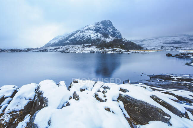 Small mountain surrounded by low clouds by one of the upper lakes in killarney with snow covered rocks in the foreground, Killarney National Park; County Kerry, Ireland — Stock Photo