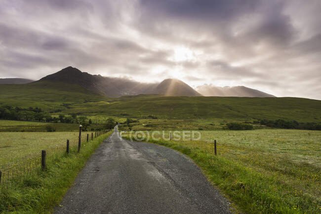 Vista lungo una strada al mattino presto con il sole che sorge dietro la cresta nera della cuillina; Glen Brittle, Skye, Scozia — Foto stock