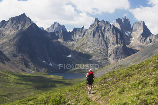 Female Hiker Walking On Mountain Trail With Mountain Lake, And Valley With Clouds And Blue Sky; Yukon, Canada — Stock Photo