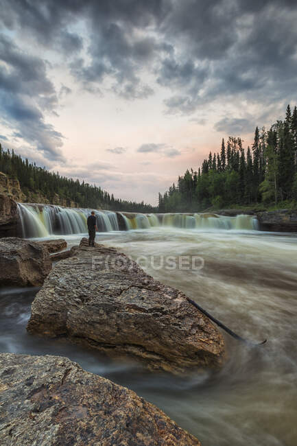 Людина дивиться, як річка Троут тече через водоспади Самбаа-де-е у Територіальному парку Самба-де-е; Північно-західні території, Канада — стокове фото