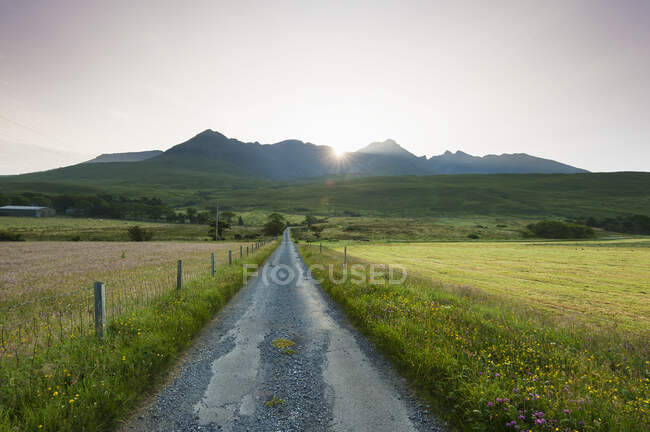 Vista lungo una strada al mattino presto con il sole che sorge dietro la cresta nera della cuillina; Glen Brittle, Isola di Skye, Scozia — Foto stock