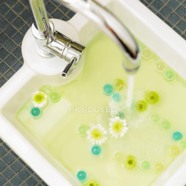 Lavello pedicure con fiori bianchi e gialli e perline da bagno Teal galleggianti in acqua; Victoria British Columbia, Canada — Foto stock