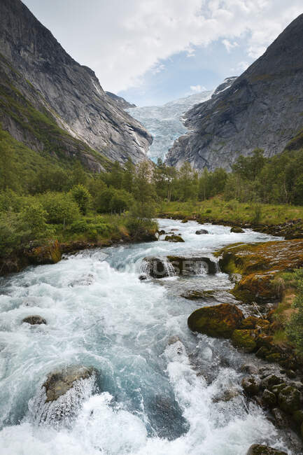 Acqua che scorre in un fiume in una valle di alberi tra le montagne; Olden, Norvegia — Foto stock
