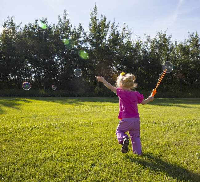 Chica joven corriendo en un parque haciendo burbujas; St. Albert, Alberta, Canadá - foto de stock