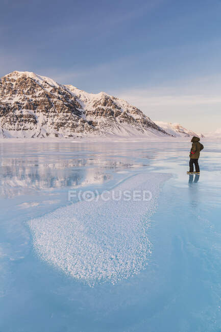 Homme dans un parka debout sur la glace de débordement sur la rivière Anaktuvuk gelée, cristaux de gel Hoar au premier plan, montagne Napaktualuit en arrière-plan, portes du parc national de l'Arctique ; Alaska, États-Unis d'Amérique — Photo de stock