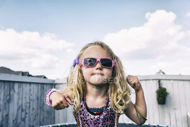 Девушка с кудрявыми светлыми волосами, солнцезащитные очки и украшения, стоящие на батуте на заднем дворе; Spruce Grove, Альберта, Канада — стоковое фото