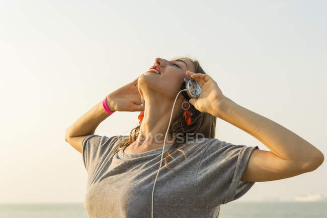 Jeune femme écoutant de la musique avec ses écouteurs sur la plage ; Xiamen, Chine — Photo de stock