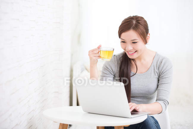 Woman using  laptop and holding cup — Stock Photo