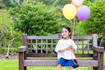 Kleines Mädchen auf Parkbank mit Luftballons. — Stockfoto