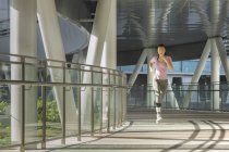 Una giovane donna asiatica sta facendo jogging attraverso la città di Singapore la mattina presto. Supera una sezione di architettura in acciaio e vetro . — Foto stock