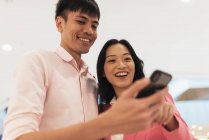Приваблива молода азіатська пара ділиться смартфоном разом — стокове фото