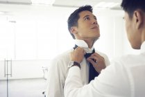 Hombre ayudando con corbata a guapo asiático empresario - foto de stock