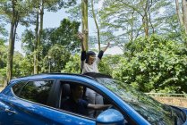 Junge Frau steht durch die Öffnung eines Schiebedaches auf einem Auto — Stockfoto