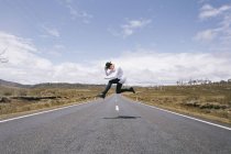 Young male traveler jumping on the road — Stock Photo