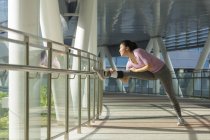 A young asian woman is stretching before her daily running workout in Singapore — Stock Photo