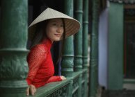 В'єтнамська жінка, що носить В'єтнамську капелюх стоячи на балконі у Хой послугами в її Ао Dai — стокове фото