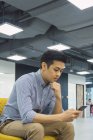 Молодий азіатський бізнесмен використовує смартфон в сучасному офісі — стокове фото