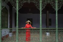 Vietnamita con un cappello conico in piedi su un balcone a Hoi An nella sua Ao Dai — Foto stock