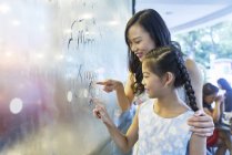 Young asian woman and girl painting on glass in mall — Stock Photo