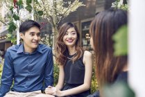 Compagnia di giovani amici asiatici insieme seduti su panchina — Foto stock