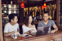 Young asian friends using laptop together in bar — Stock Photo