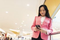Jeune attrayant asiatique femme en utilisant smartphone dans le centre commercial — Photo de stock