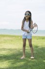 Young girl in sunglasses playing badminton on beach — Stock Photo