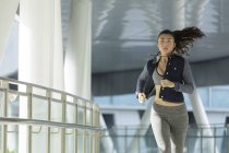 Eine junge asiatin joggt frühmorgens durch die stadt singapore. Sie passiert einen Abschnitt aus Stahl und Glas. — Stockfoto