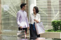 Joven casual asiático pareja con bolsas en compras en mall - foto de stock