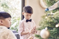 Happy asian boys decorating christmas fir tree together — Stock Photo