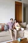 Mature asian casual couple sitting on sofa at home and watching tv — Stock Photo