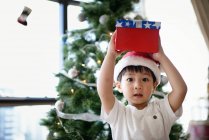 Asian family celebrating Christmas holiday, boy holding christmas gift on head — Stock Photo