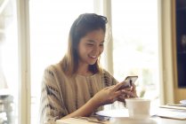 Jeune jolie asiatique femme en utilisant smartphone dans café — Photo de stock